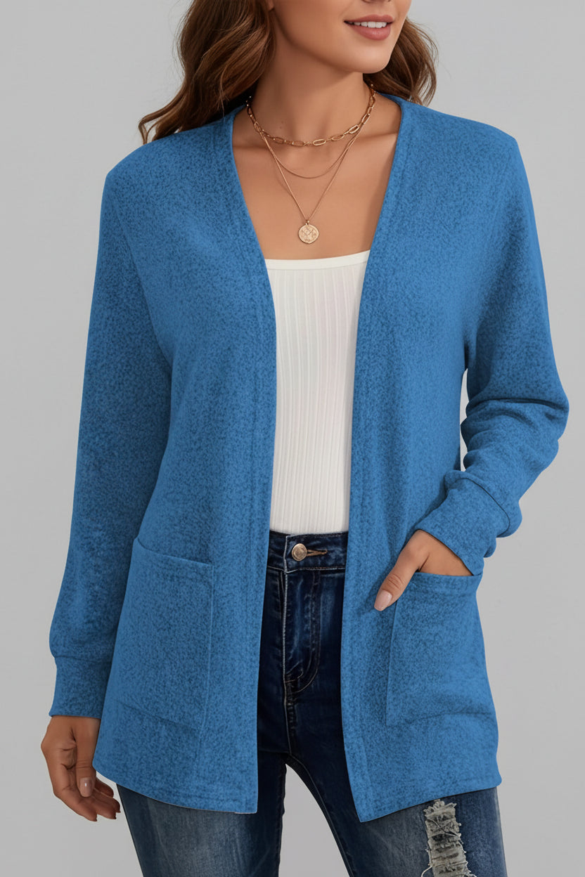 A woman wearing a blue open-front cardigan with front patch pockets over a white ribbed tank top and dark blue jeans.