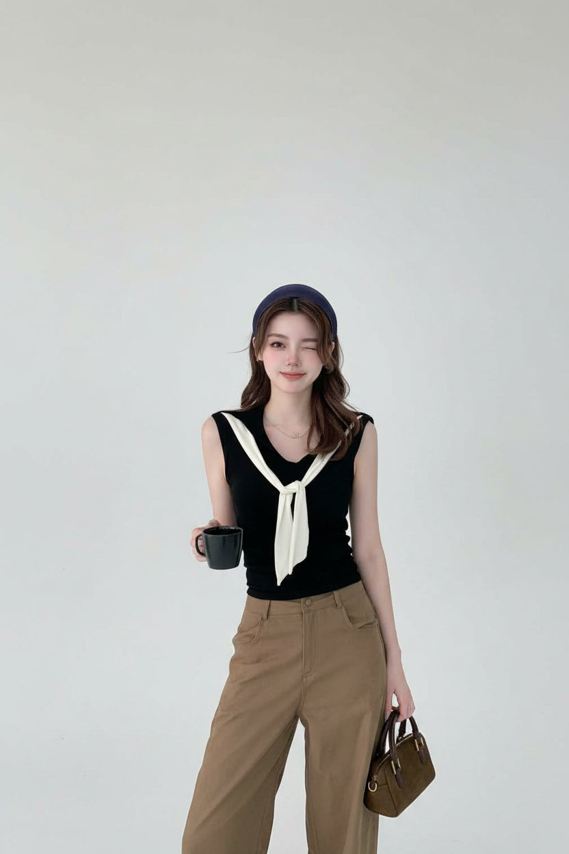 Woman in a stylish outfit with a black top and beige pants, holding a brown handbag in a modern interior setting.