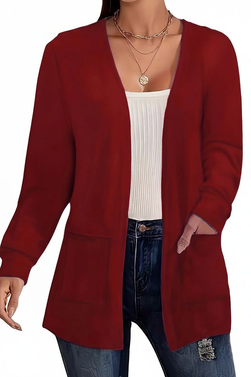 A woman wearing a long-sleeve open-front cardigan in deep red over a white ribbed tank top and blue jeans, accessorized with layered gold necklaces.