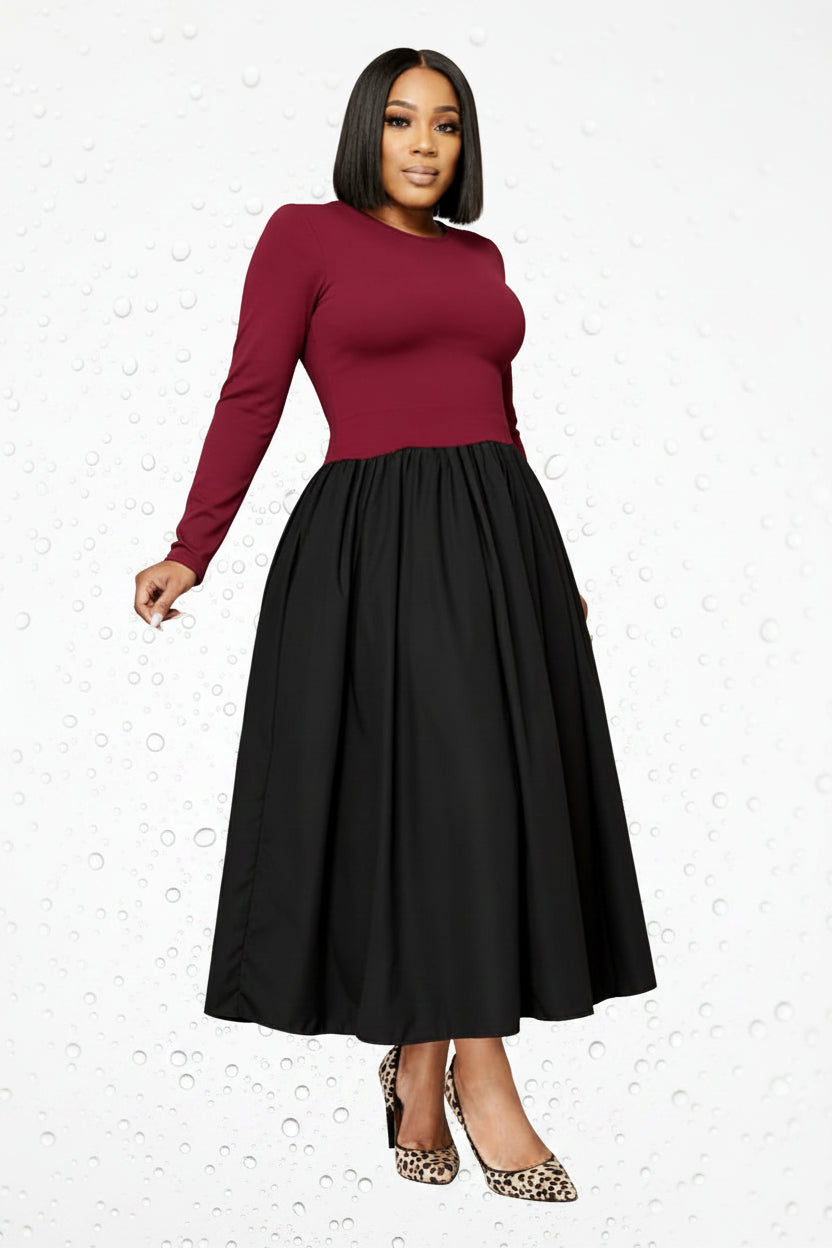 A woman models a long-sleeve midi dress with a burgundy top and a full black skirt, paired with leopard print heels, standing in front of a white cabinet.