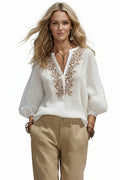 White blouse with intricate brown embroidery worn by a person against a neutral background