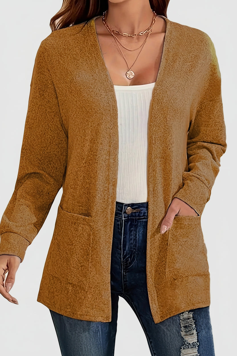 Person wearing a brown cardigan over a white top and blue jeans with a blurred indoor background.