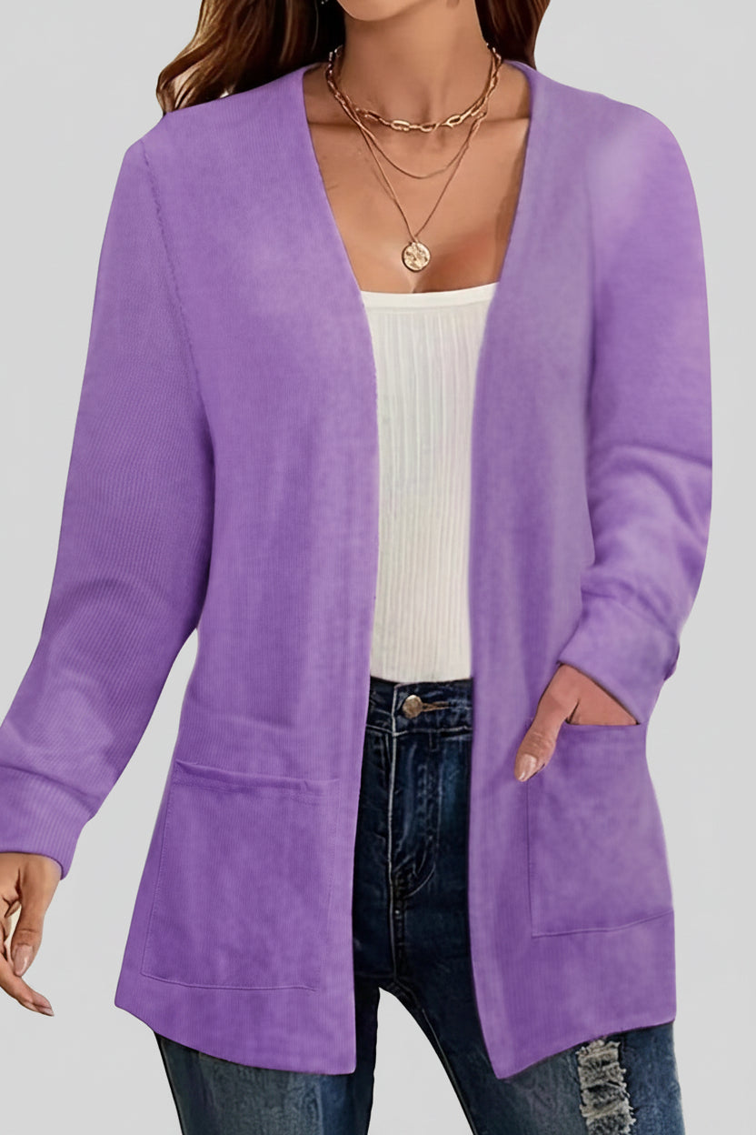 Person wearing a purple cardigan over a white top and jeans, with a blurred indoor background.