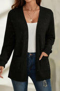 Person wearing a black cardigan over a white top and blue jeans on a neutral background