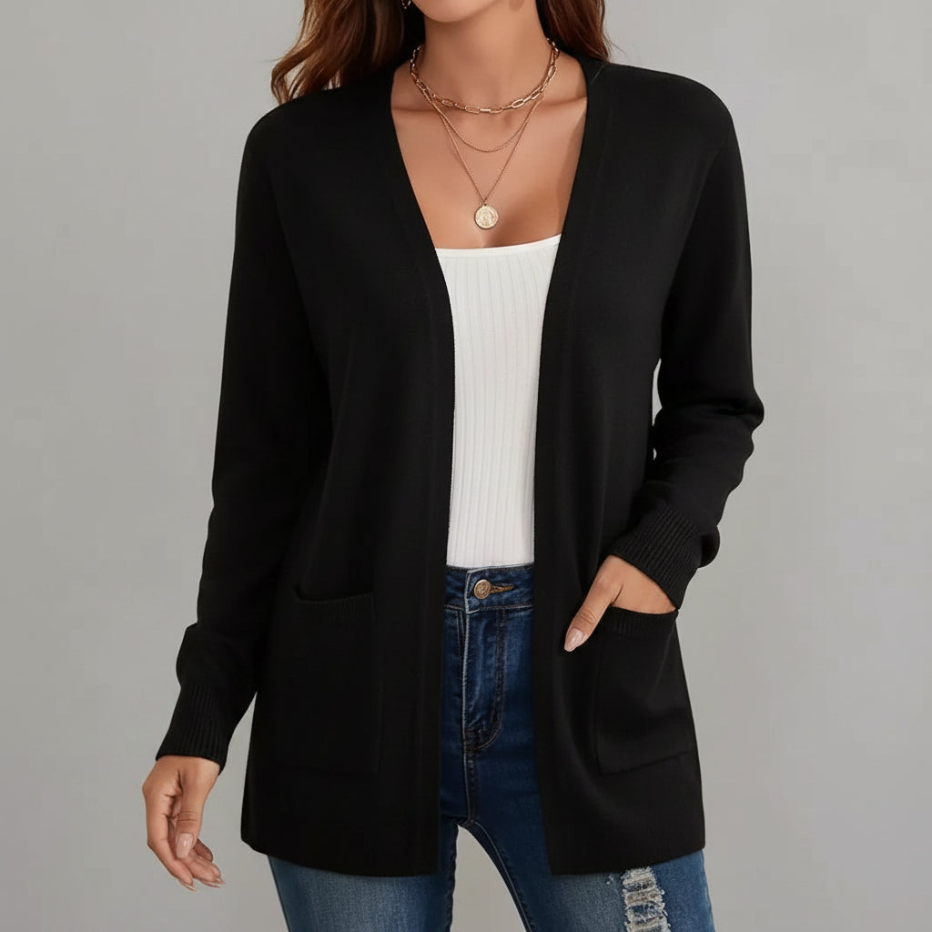 Person wearing a black cardigan over a white top and blue jeans, standing against a neutral background.